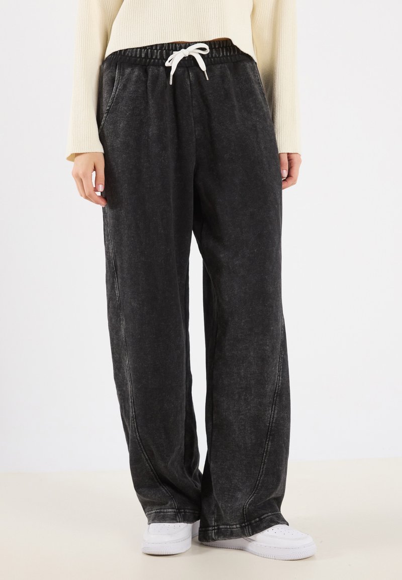 Zwarte, losvallende sweatpants met een gestructureerde afwerking, elastische tailleband en witte koord. Zijzakken en zichtbare stikseldetails.