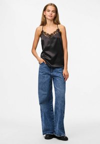 Crna satenasta majica na bretele s čipkastim detaljima, u kombinaciji s svijetloplavim širokim trapericama. Odjeća ima elegantnu siluetu i ležeran dizajn.