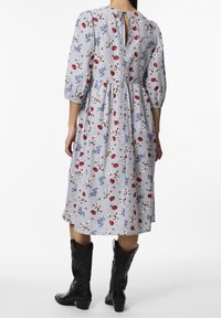 Kukallinen, raidallinen mekko, jossa on 3/4 puffihihat, kireä vyötärö ja avonainen selkä, yhdistettynä mustiin cowboy-kengänsä.