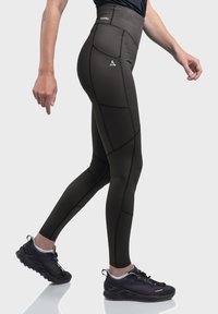 Hochtaillierte, dunkelgrüne Sportleggings mit kontrastierenden schwarzen Nähten und einem Logo am Bund, kombiniert mit schwarzen Sportschuhen.
