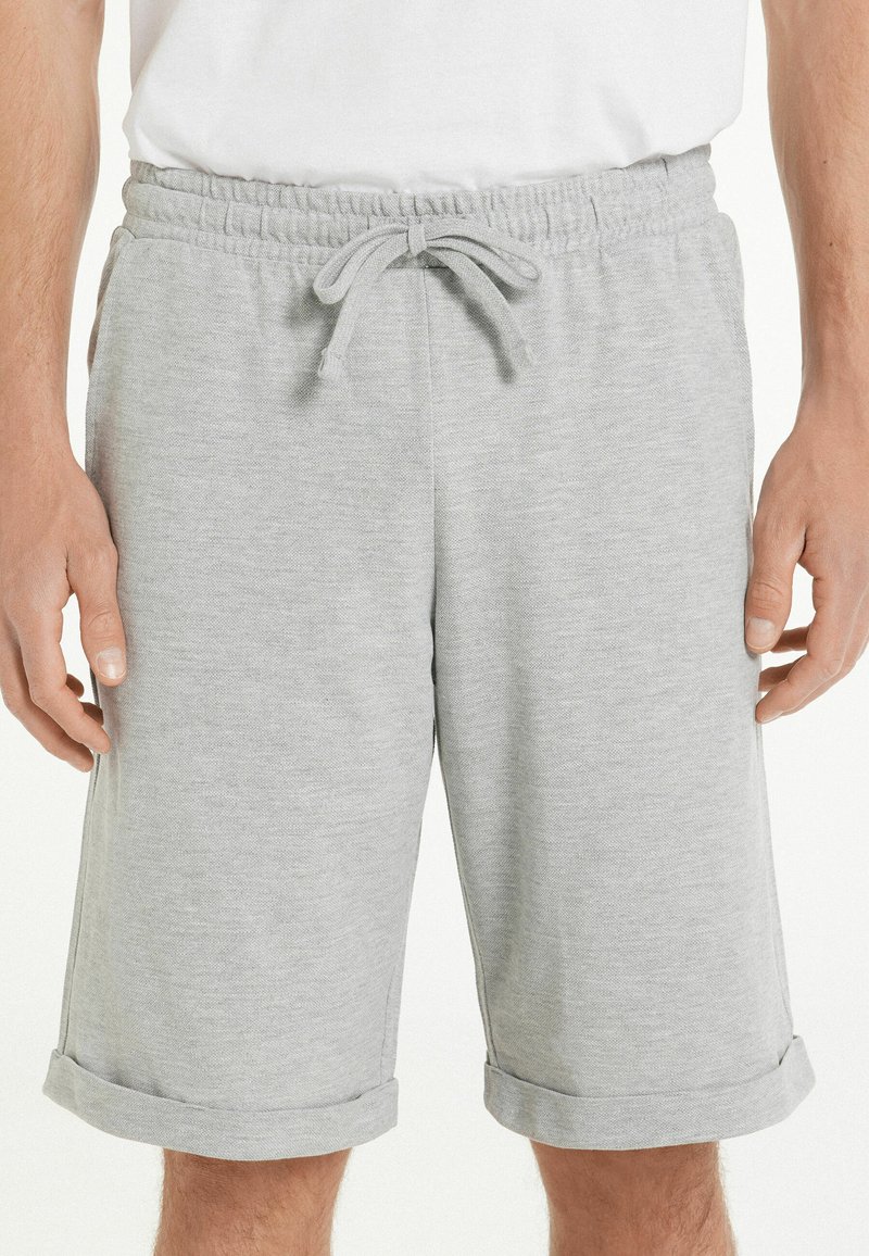 Pantalones cortos de algodón grises con cintura elástica, cordón ajustable y dobladillos enrollados. La tela tiene una textura suave y lisa.