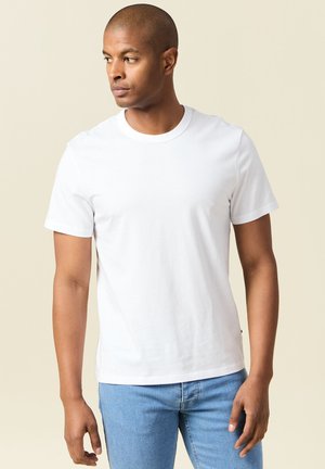 Camiseta blanca de manga corta con escote redondo, hecha de algodón, con una textura suave, combinada con vaqueros de mezclilla azul claro.