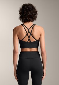 Reggiseno sportivo nero con spalline incrociate, tessuto elastico e design aderente. Abbinato a leggings neri a vita alta.