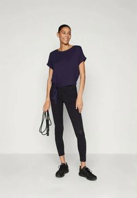 Marinblå kortärmad topp med sidoknut, kombinerad med svarta leggings och svarta sneakers. Tyget ser mjukt ut med en avslappnad passform.