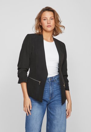 Black blazer with a tailored design, features zippered side pockets, and three-quarter sleeves. Worn over a white top and blue jeans.