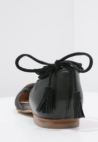 Czarne skórzane płaskie buty z zamkniętą piętą, ozdobnymi frędzlami na sznurowadłach związanych w kokardę oraz plecionym detalem po boku.