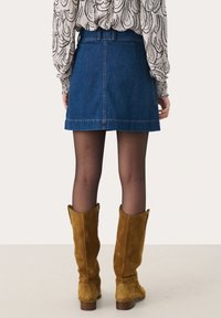 Tummansinisestä denim-minihameesta, jossa on suora leikkaus, siisti helma ja kontrastiväriset ompeleet. Yhdistetty ruskeisiin mokkanahkasaappaisiin polvipituisina.