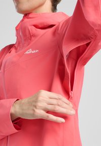 Giacca impermeabile di un brillante colore rosa, con cappuccio regolabile, tasche laterali con cerniera e una texture di tessuto leggera e liscia.