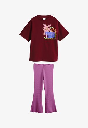 Weinrotes Kurzarmhemd mit "Tropical Sunset"-Aufdruck und Palmenmotiv, kombiniert mit ausgestellten lavendelfarbenen Hosen.