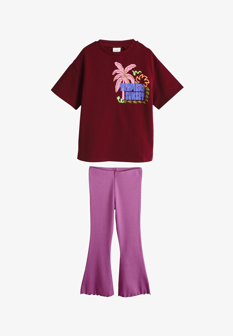 Burgundska srajca s kratkimi rokavi z motivom "Tropski sončni zahod" in palmami, v kombinaciji z razširjenimi sivkasto vijoličnimi hlačami.