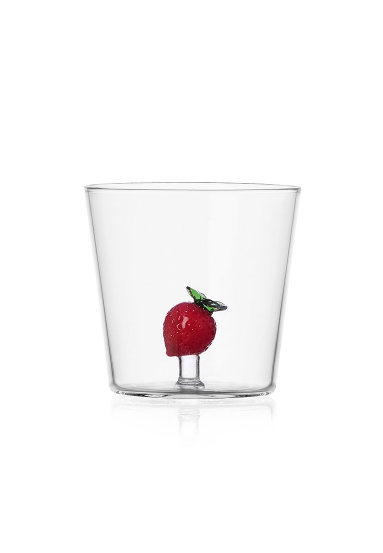 Przezroczysty szklany kubek z czerwonym truskawką i zielonym listkiem, ustawiony na małym piedestale wewnątrz kubka. Gładka tekstura, prosta forma.