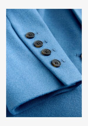 Light blue wool fabric with a textured surface; features four dark buttons along the cuff and contrasting thread stitching.