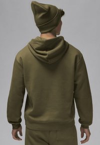 Felpa verde oliva dal taglio rilassato, con un ampio cappuccio e orlo a coste. Abbinata a un berretto verde oliva coordinato. Tessuto morbido.