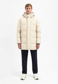 Beige gewatteerde jas met een capuchon, voorzien van een geruit ontwerp en zwarte accenten. Draag het over donkere broeken en lichte sneakers.