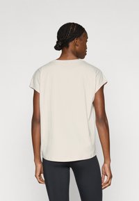 Μπεζ κοντομάνικη μπλούζα με στρογγυλή λαιμόκοψη και άνετη γραμμή. Ομαλή υφή, ίσιες ραφές και διακριτικά καμπυλωτό τελείωμα. Φοριέται με μαύρο κολάν.