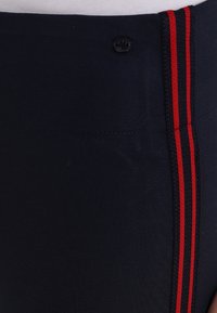 Marinblå träningbyxor med röda sidostreck, tillverkade av stretchigt material. Har en liten knapp på midjebandet. Texturen verkar slät.