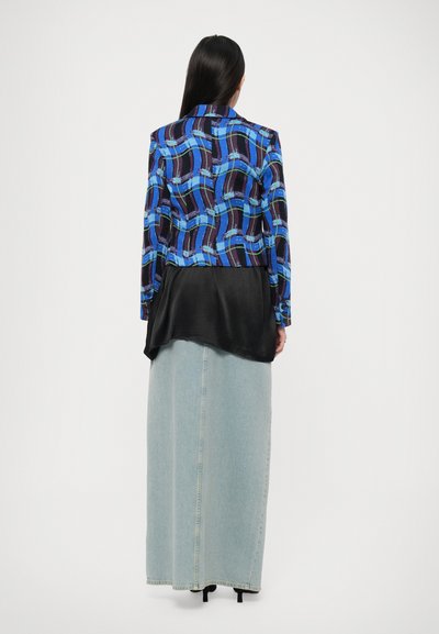 Giacca a maniche lunghe blu e nera a motivo, sovrapposta a un pannello inferiore in satin nero, abbinata a una gonna lunga in denim chiaro.