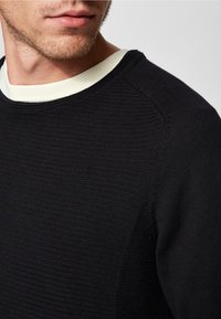 Pull noir texturé avec un col rond, arborant un motif côtelé subtil et un col intérieur en couleur claire contrastante.