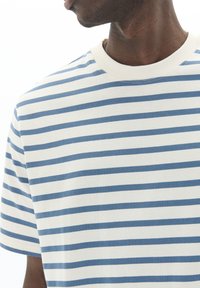Striped short-sleeve t-shirt in white and light blue, featuring a crew neckline and soft cotton texture. Horizontal stripes across the fabric.