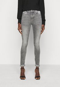 Jeans skinny cinzentos com um fecho de cinco botões, ligeiro desgaste, mangas enroladas e uma textura de denim suave, combinados com saltos altos pretos com tiras.