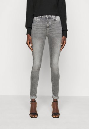 Jeans skinny cinzentos com um fecho de cinco botões, ligeiro desgaste, mangas enroladas e uma textura de denim suave, combinados com saltos altos pretos com tiras.