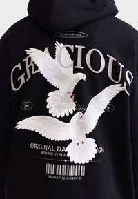 Sweatshirt preto com grande gráfica branca de duas pombas com detalhes em vermelho. O texto diz "GRACIOSO" e "RBL Redefined Rebel." Código de barras abaixo do design.