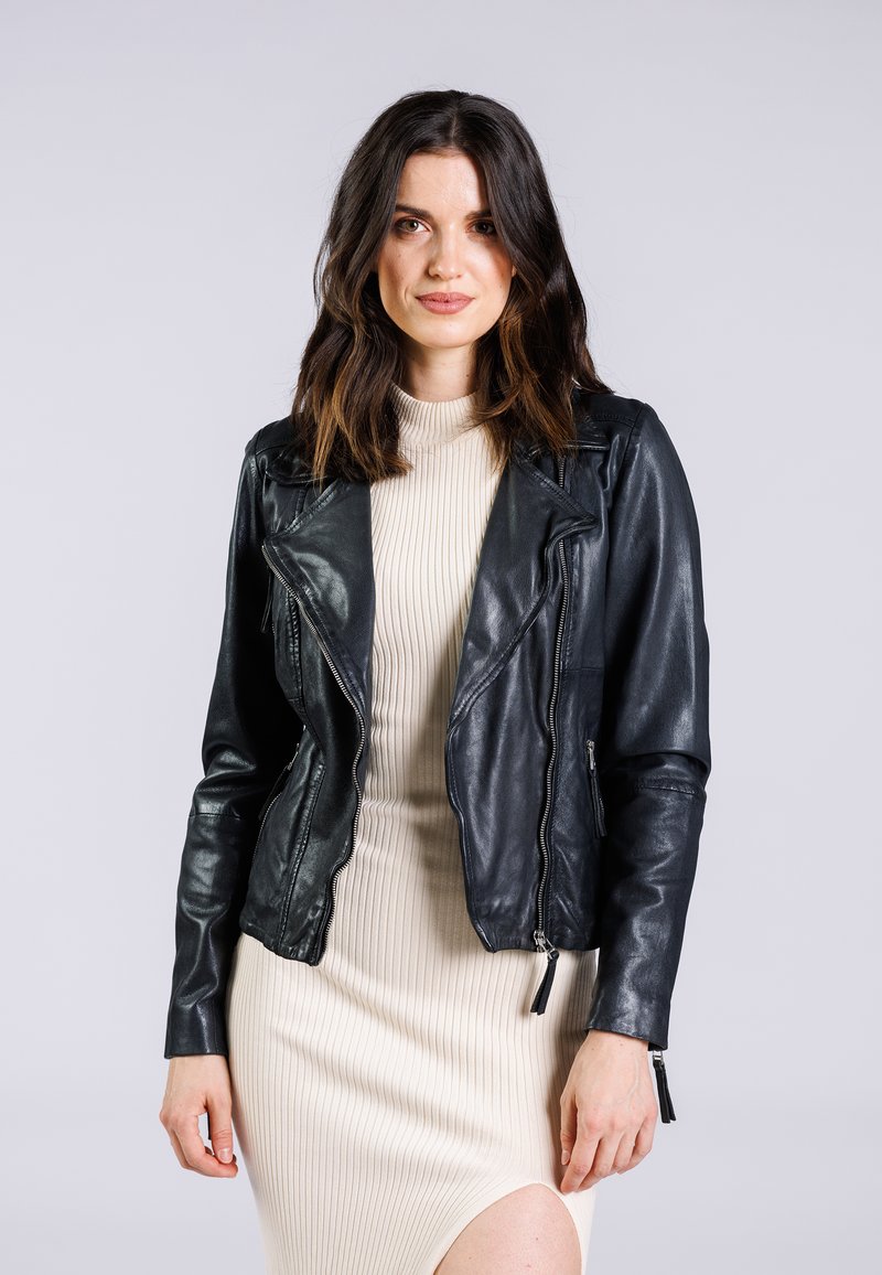 Schwarze Leder-Bikerjacke mit asymmetrischem Reißverschluss, auffälligen Revers und strukturierter Oberfläche, getragen über einem cremefarbenen gerippten Kleid.