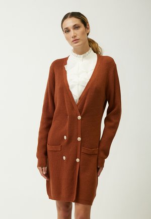 Cardigan lungo color ruggine realizzato in tessuto a maglia testurizzata. Presenta un profondo scollo a V, bottoni frontali e due tasche applicate.
