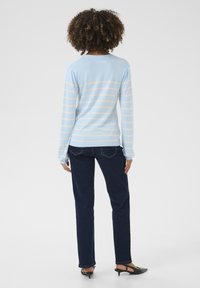 Pull rayé bleu clair à manches longues, en tissu doux et avec un col rond, associé à un jean bleu foncé et des chaussures à talons noires.
