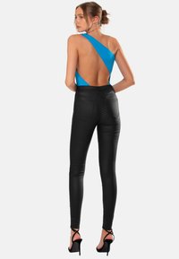 Enaxlad blå bodysuit med utskärningsdesign, i kombination med höga svarta skinny jeans och svarta remsandaler. Släta material genomgående.