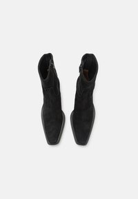 Botines de ante negros hasta el tobillo con un diseño de punta afilada, que cuentan con un cierre lateral y una textura suave y mate.