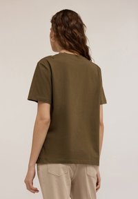 Camiseta de algodón verde oliva con mangas cortas, corte relajado y adornos en los hombros. Textura suave, escote redondo.