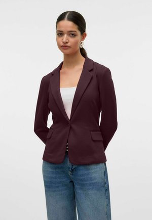 Burgunderfarget blazer med klaffelapper, frontlommer, strukturert design, kombinert med en hvit topp og lyseblå denimjeans.