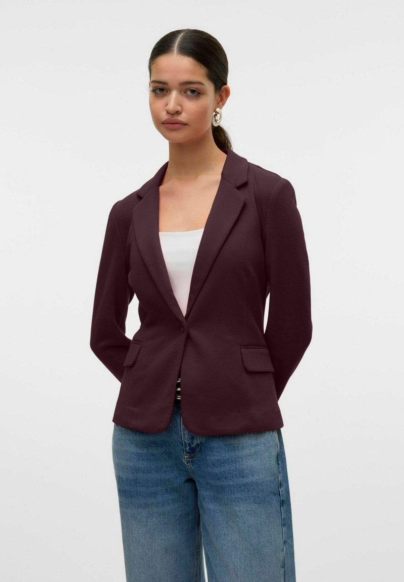 Burgundský blazer s klopovými límci, předními kapsami, strukturovaným designem, spárován s bílým topem a světlými modrými džíny.
