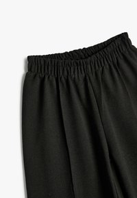 Zwarte stoffen broek met een verzamelde elastische tailleband. De textuur is zacht en glad, met een rechte snit en zonder zichtbare patronen of accenten.