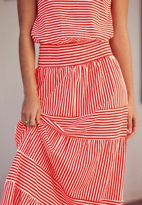 Röd- och vitrandig tvådelad outfit som består av en lös topp och en lager-på-lager kjol. Tyget är lätt och har en synlig struktur.