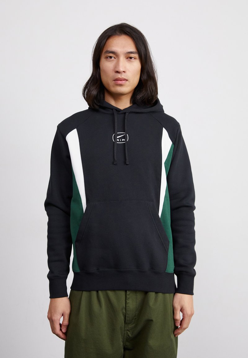 Mustapaitapaita, jossa on valkoisia ja vihreitä paneeleita, etutasku ja narusysteemi huppua varten. Materiaali näyttää pehmeältä ja rento istuvuus.