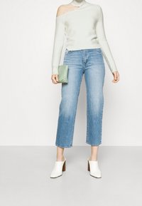 Light green, ribbed, off-the-shoulder sweater; high-waisted blue denim jeans; cream chunky heeled mules; holding a mint green pouch.