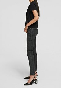 Camiseta negra de manga corta combinada con jeans ajustados de color gris oscuro que presentan una textura brillante, y tacones negros de altura hasta el tobillo con acentos metálicos.