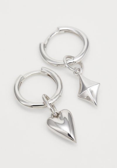 Silberne Creolen mit einem herzförmigen und einem diamantförmigen Anhänger, beide poliert und reflektierend, mit einer glatten Oberflächenstruktur.