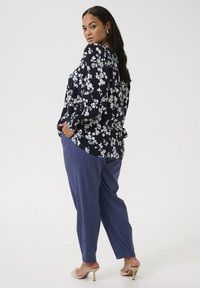 Bluză bleumarin cu model floral, cu mâneci bufante, asortată cu pantaloni largi albastre și sandale bej cu vârf deschis. Textură de țesătură netedă vizibilă.