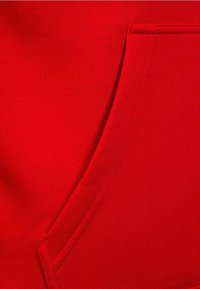 Tessuto di felpa rossa con una texture morbida, con tasca frontale e un design pulito e semplice. Le cuciture sono dello stesso colore rosso.