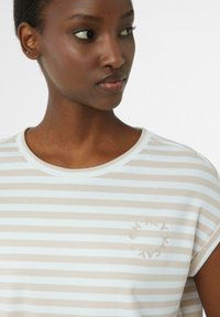 Gestreiftes Baumwoll-T-Shirt in Beige und Weiß, mit Rundhalsausschnitt und umgeschlagenen Ärmeln. Es hat ein kleines, rundes Logo "HEY VACAY" auf der Vorderseite.