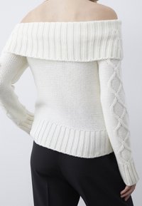 Weißer schulterfreier Pullover mit geripptem Ausschnitt und Zopfmusterärmeln, mit einem strukturierten Strickmuster und einem taillierten Bund.