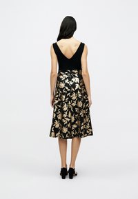 Μαύρο φόρεμα με βαθιά V-πλάτη, με φούστα μήκους μέχρι το γόνατο διακοσμημένη με χρυσά λουλουδάτα σχέδια σε μαύρο φόντο, λεία υφή.