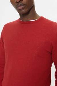 Pulover roșu cu mâneci lungi, tricotat, cu guler striat și țesătură texturată, cu croială aproape de corp și design minimalist.