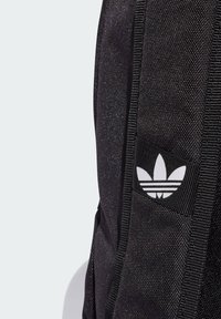 Black fabric backpack with textured surface, featuring a white Adidas logo and sturdy straps. Simple design, practical for everyday use.