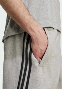 Grijze jersey t-shirt gecombineerd met grijze sweatpants met drie zwarte verticale strepen. Zak zichtbaar met ritsdetail. Zachte textuur.