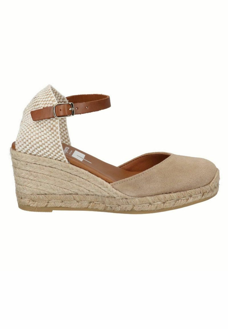 Sandalo con zeppa in suede beige, dotato di cinturino alla caviglia intrecciato e suola in juta. Presenta una punta arrotondata e un cinturino regolabile marrone.