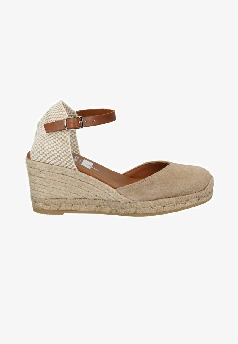 Sandalo con zeppa in suede beige, dotato di cinturino alla caviglia intrecciato e suola in juta. Presenta una punta arrotondata e un cinturino regolabile marrone.